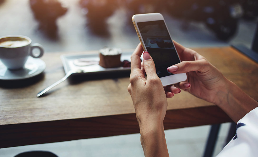 Woman at cafe taking photo of coffee on phone