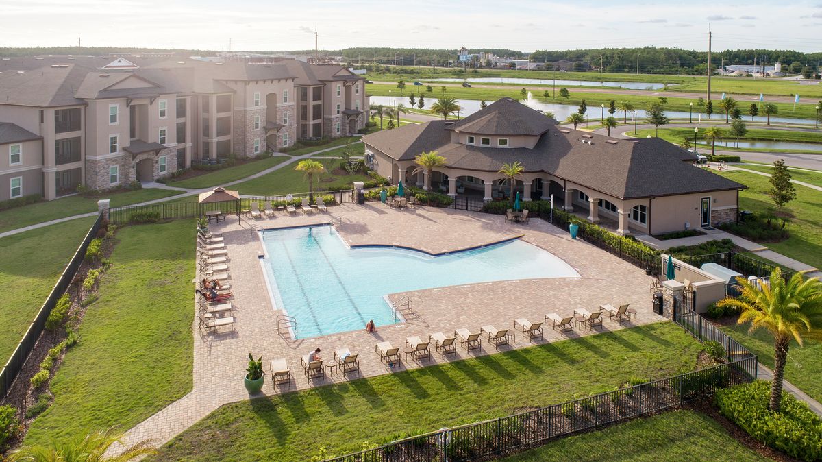 Angled aerial view of the lap pool, backside of the clubhouse, and pond with a fountain
