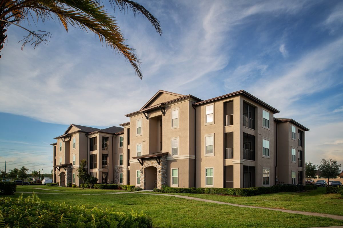 Apartment building exterior with landscaped grass areas and a cloudy sky