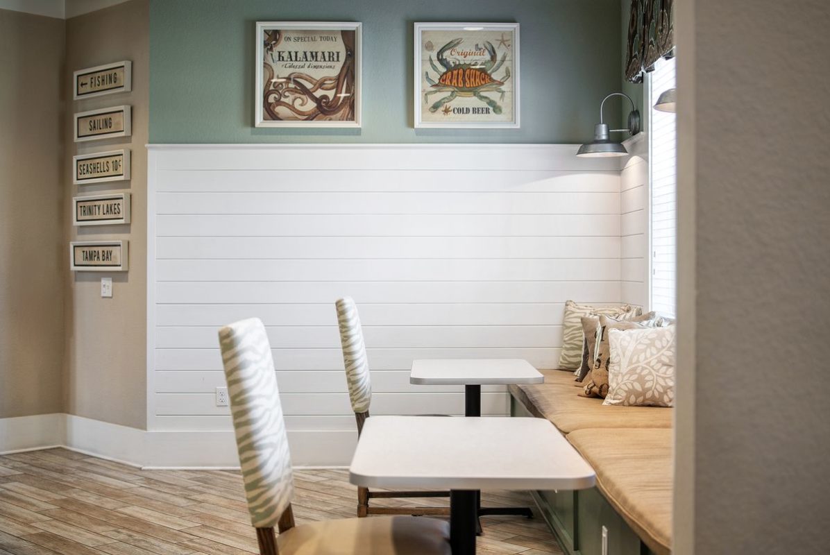Seating area with two tables that each have one chair on one side and share a long bench under a window on the opposite side