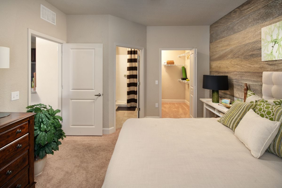 Furnished apartment bedroom with carpet flooring, and access to a walk-in closet and private bathroom with tile flooring