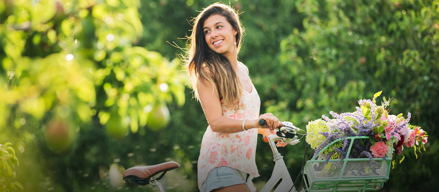 Woman walking with bike that has a basket of flowers